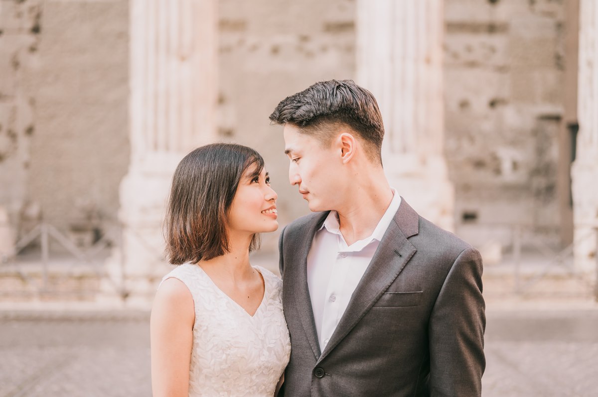 A couple shares a romantic gaze in front of ancient Roman columns, capturing the charm of a wedding experience in Italy