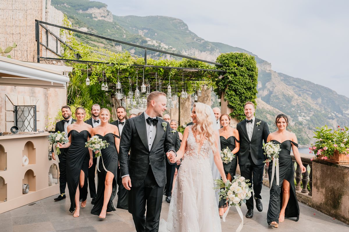 Elegant Bride, Groom, and Wedding Party in Positano A chic bridal party walks along a terrace during a villa magia wedding positano, with the bride and groom smiling at each other