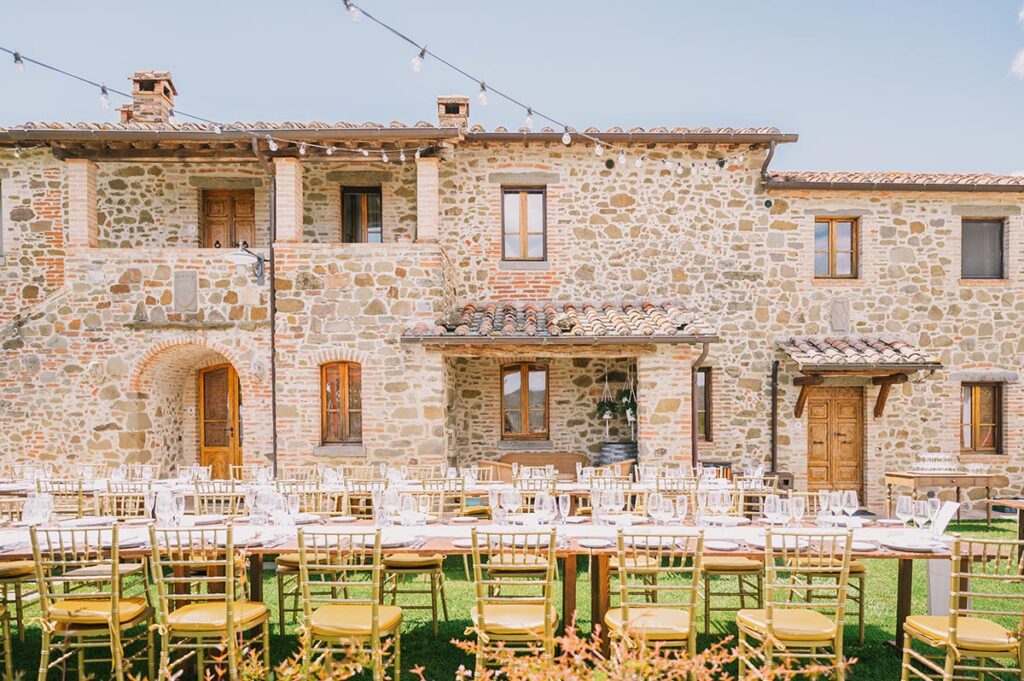 A Chianti Wedding Planner sets up a stunning outdoor reception with elegant tables in front of a rustic Tuscan stone villa