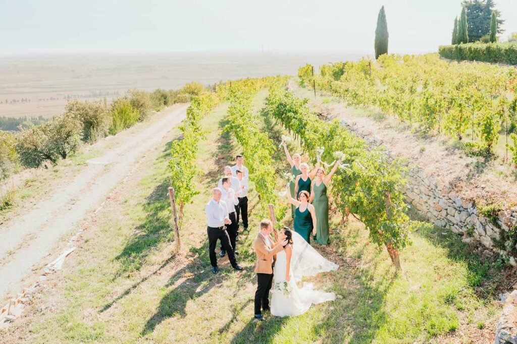 A joyful wedding celebration in a sunlit Tuscan vineyard, with the bride, groom, and their guests raising glasses in a beautifully planned event by a Tuscany wedding planner
