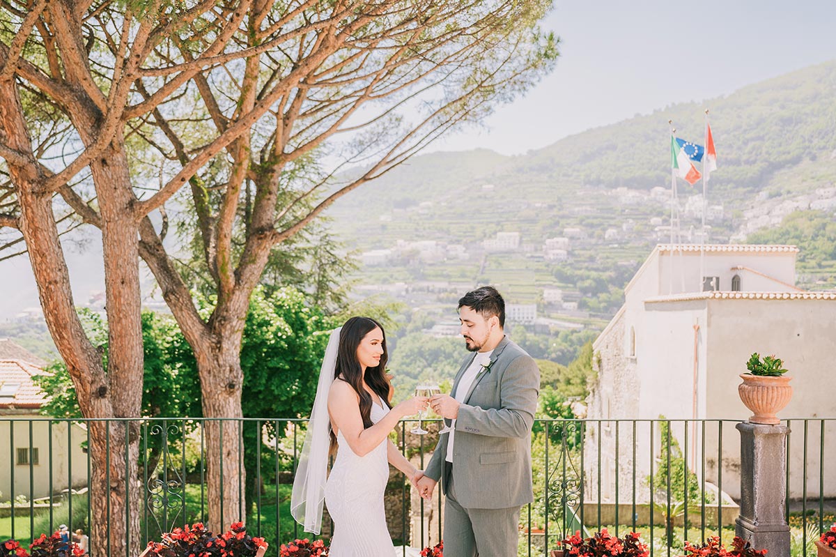 Wedding Champagne Toast with a View A bride and groom share a champagne toast on a terrace overlooking the hills, celebrating their Palazzo Confalone wedding Ravello