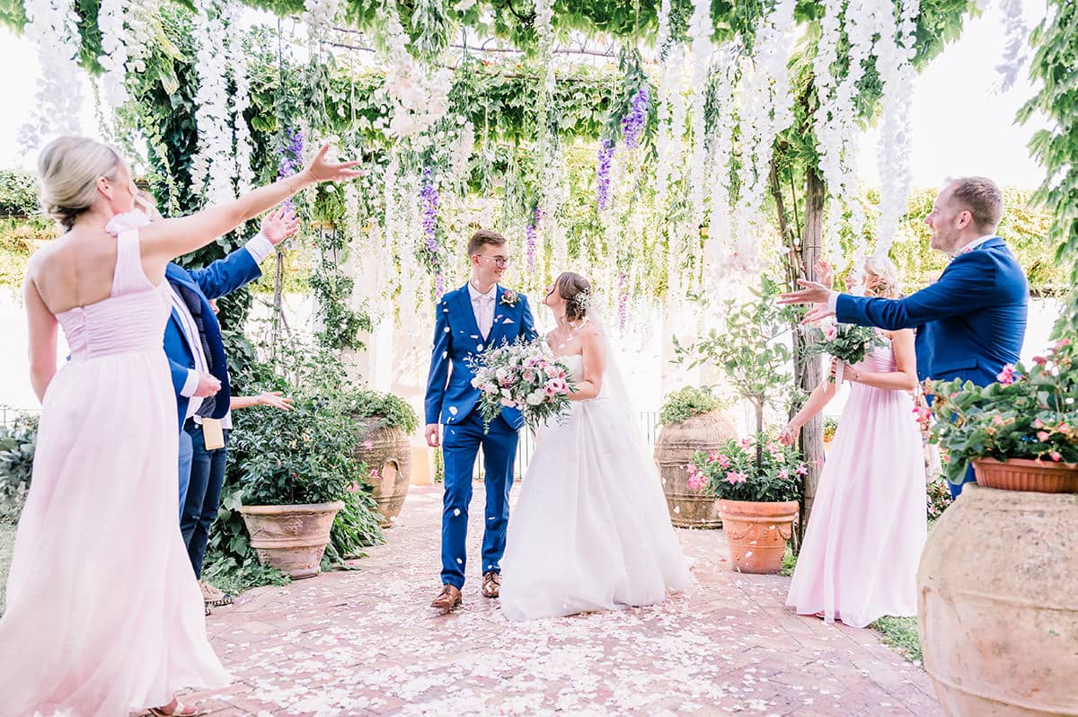 Celebratory Confetti Toss at a Garden Wedding Guests joyfully toss confetti over the newlyweds under a stunning wisteria pergola at a Palazzo Confalone wedding Ravello