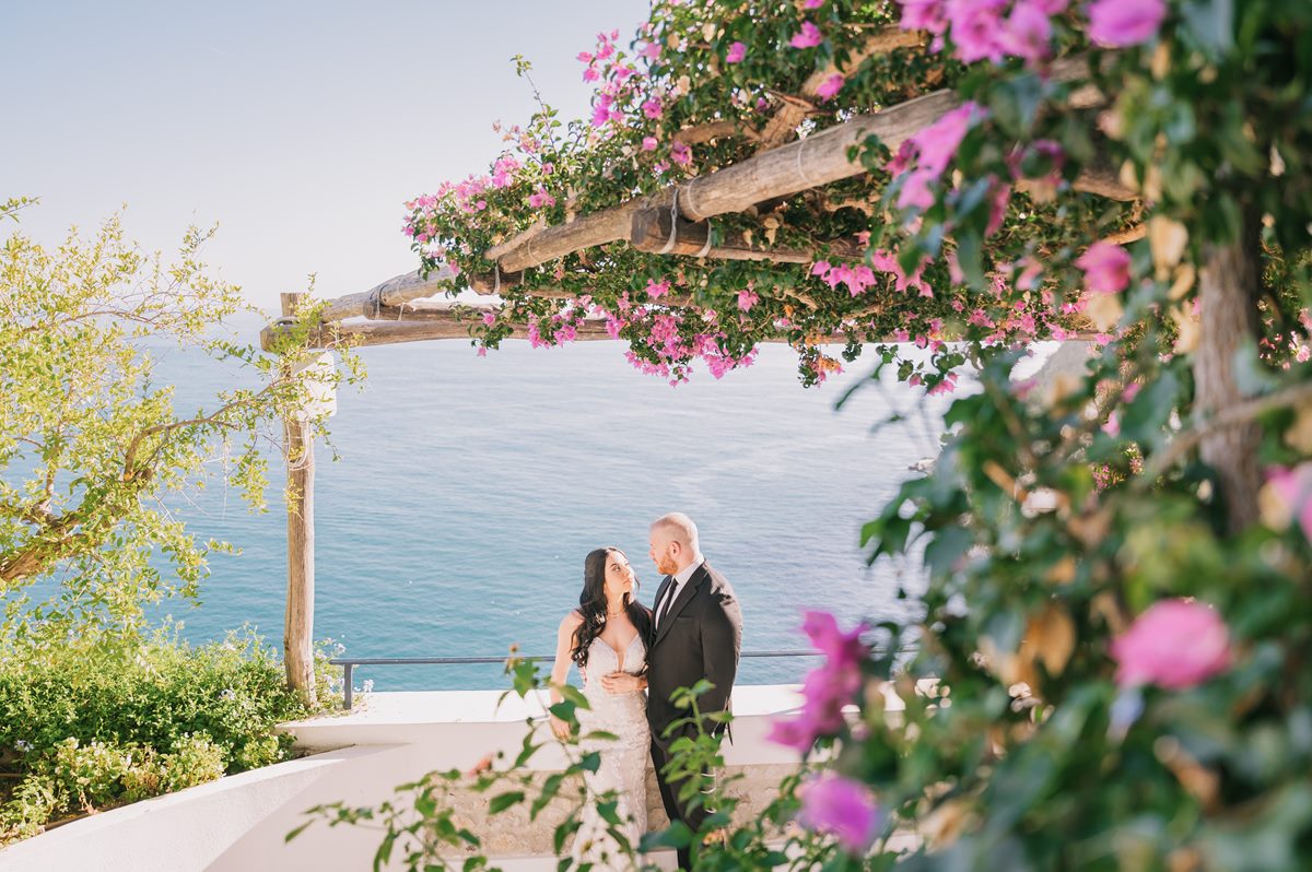 Bride and groom exchanging vows under a pergola with blooming flowers and sea views, crafted by a wedding planner in Positano