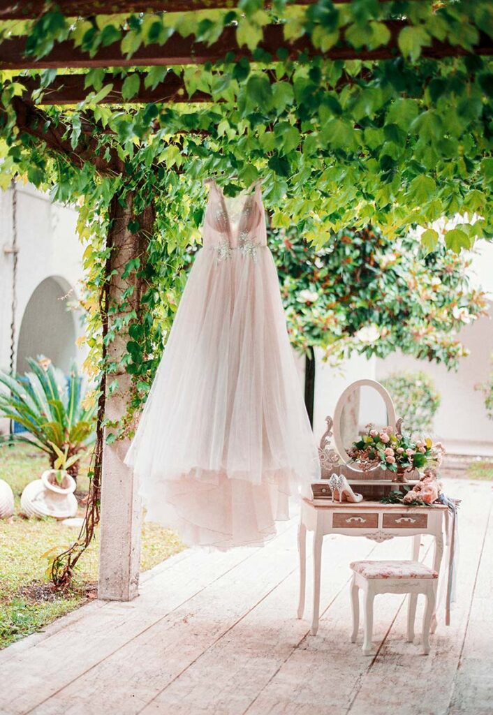 A wedding dress hangs from a vine-covered pergola in a stunning Chianti wedding venue, with an elegant bridal setup