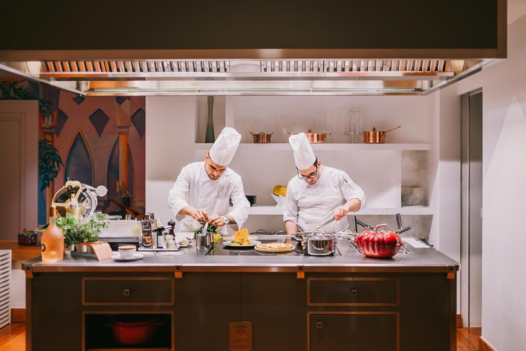 Two professional chefs in white uniforms prepare gourmet dishes in an elegant Italian kitchen, showcasing a luxury wedding experience in Italy
