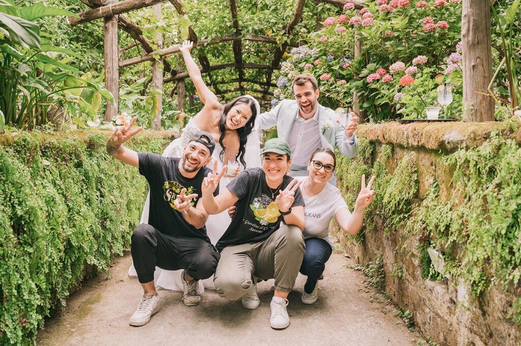 A joyful newlywed couple poses with their wedding team in a lush Italian garden, celebrating a personalized wedding experience in Italy