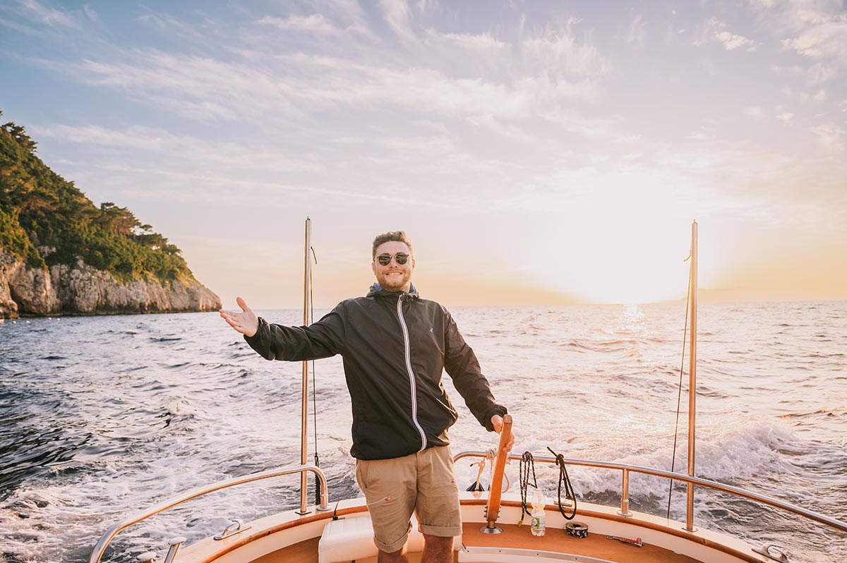 A man steers a boat along the Italian coast at sunset, embracing the beauty and adventure of a wedding experience in Italy