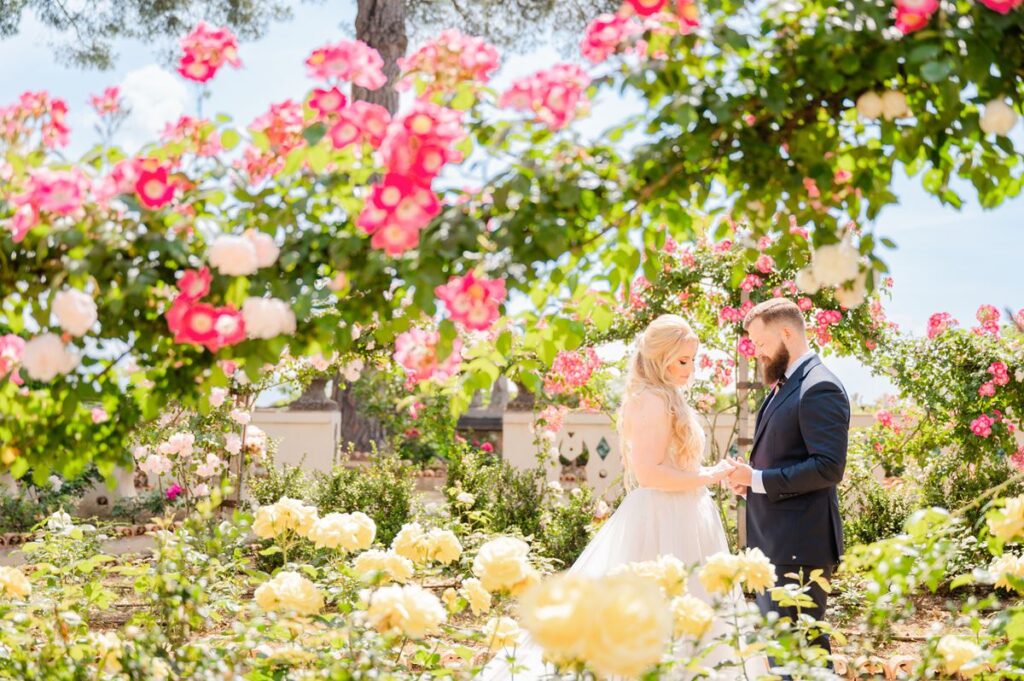 A newlywed couple shares a tender moment in a Chianti wedding venue, surrounded by blooming roses and Tuscan charm