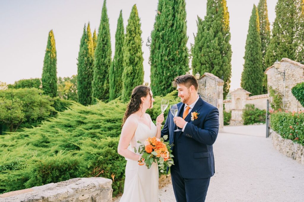 A newlywed couple toasts with champagne at a Chianti wedding venue, surrounded by lush greenery and historic stone architecture