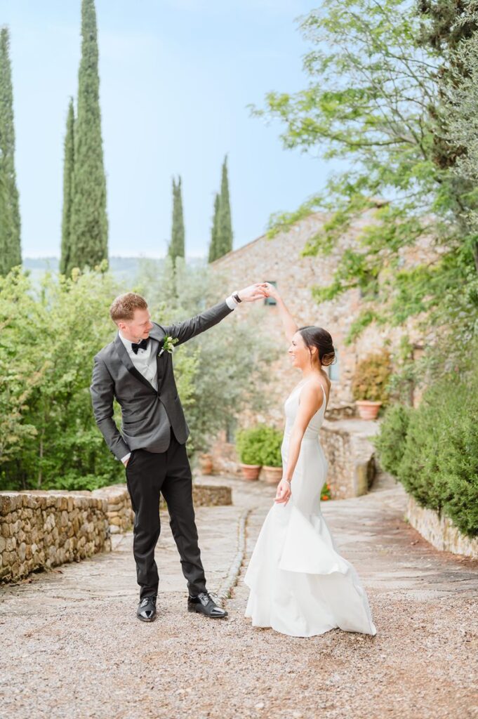 A newlywed couple dances joyfully at a Chianti wedding venue, surrounded by cypress trees and historic stone walls
