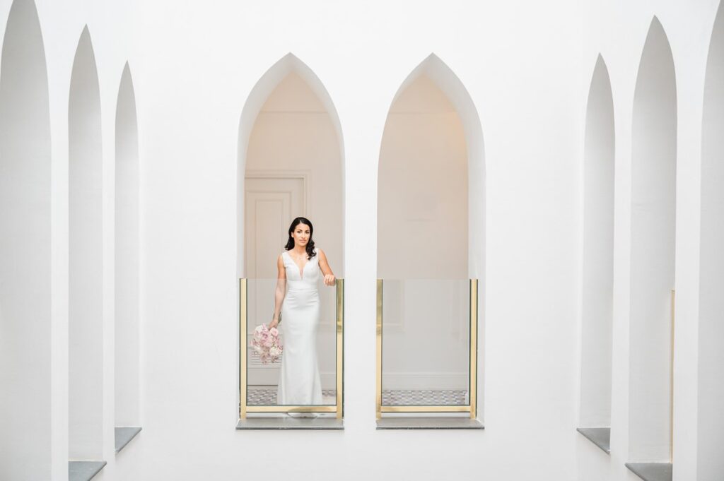 Elegant Bride Framed by Modern White Arches An elegant bride in a sleek white gown holds her bouquet, posing between modern arches during her Palazzo Avino wedding Ravello.