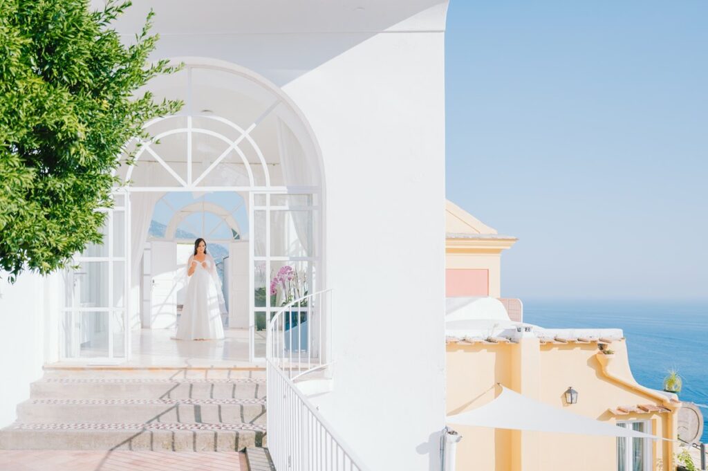 Bride in a Sunlit Archway Overlooking the Sea A serene bride in her white gown stands in a sunlit archway before her beautiful villa magia wedding positano