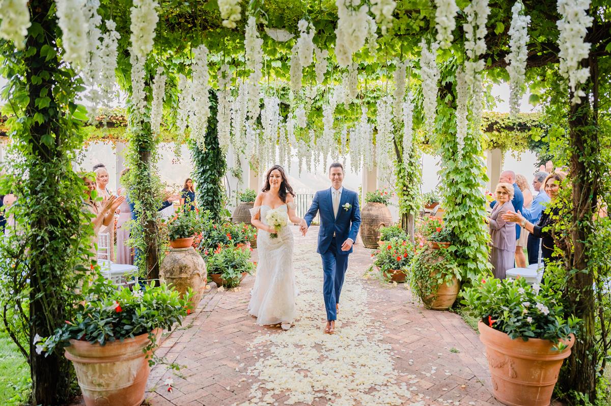 Wedding Recessional Under Wisteria in Ravello A joyful couple walks down the aisle under a cascade of wisteria, celebrating their Palazzo Confalone wedding Ravello