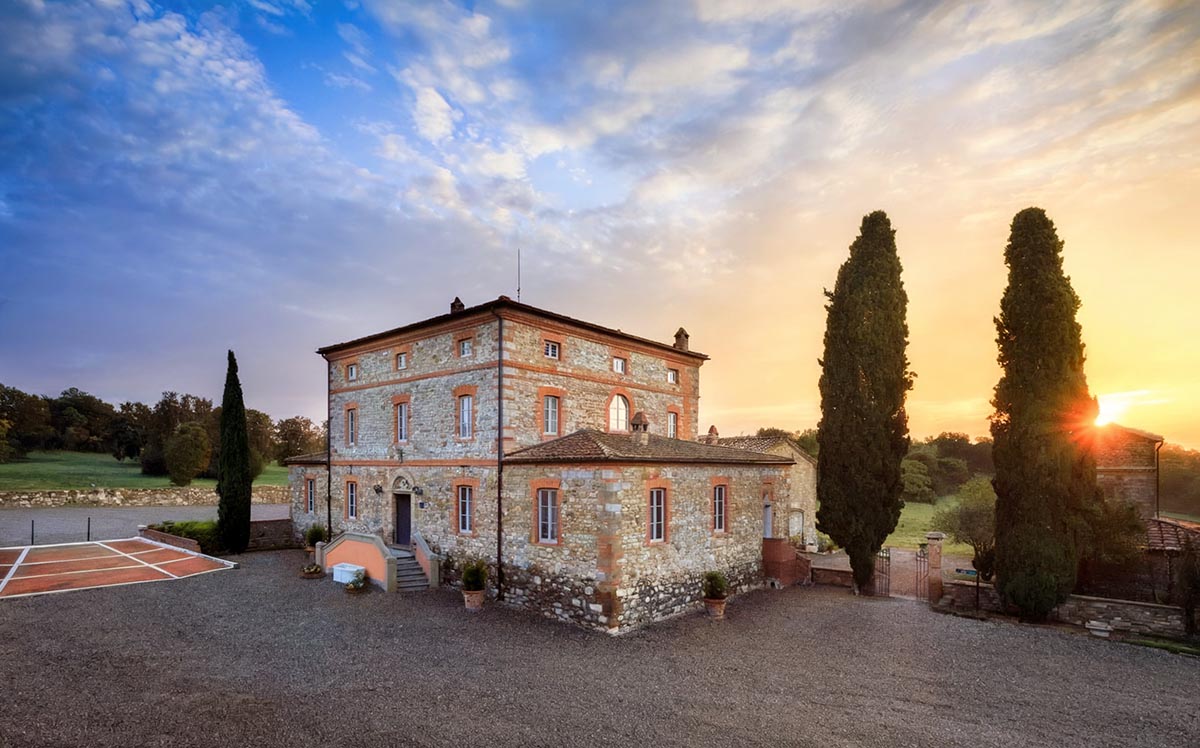 A stunning Chianti wedding venue featuring a historic stone villa, illuminated by a golden sunset with scenic countryside views
