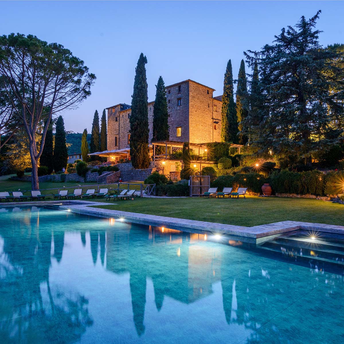 A luxurious Chianti wedding venue featuring a historic stone villa, illuminated at night, with a serene pool and lush gardens